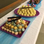 A long table for food and refreshments includes macaroons, small cakes, fruit and more.