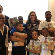 Photograph of a smiling group of people; children are holding the book "Ruth and the Green Book"
