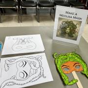 Photograph of an event station - Make a Medusa Mask setup with a black and white Medusa mask and colored markers.