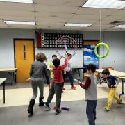Photograph shows event participants playing a game in the library with hoops and homemade shields.