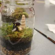 A terrarium with a toy dragon is on top of a table.