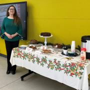 A person is standing next to a table of fruitcake and coffee.