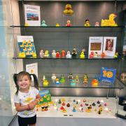 Photograph of a child smiling in front of a display case full of different rubber duckies.