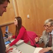 Freeman Dyson sits down as he signs the book of a man standing in front of him.