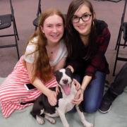 Two girls pose with a smiling puppy. 