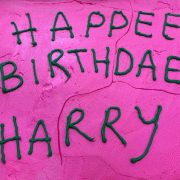 A cake with pink frosting and Happee Birthdae Harry spelled out in green frosting