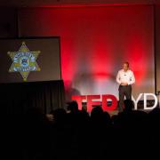 Speaker at TedxYDL next to PowerPoint presentation 