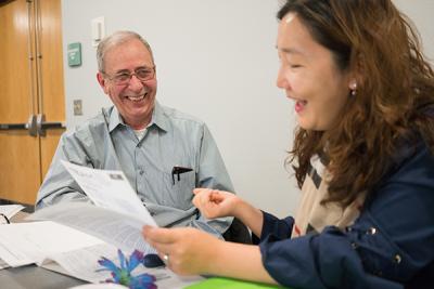 Man and woman sitting at a table looking at a document and smiling.