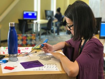 Photograph of a teen sitting at a work table working with a 3d pen to create a tactile image