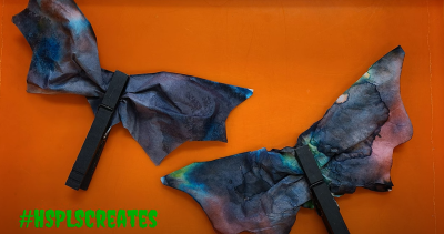 Photograph of two completed coffee filter bats. The bats are black with colorful watercolor paint.