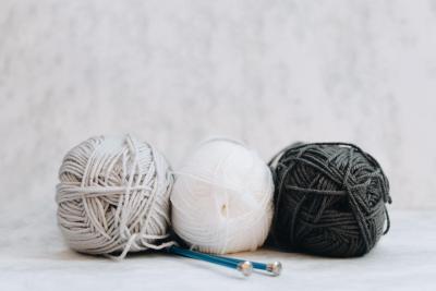 three spools of yarn, black, white and gray, sit with a pair of blue knitting needles.