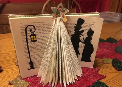 Book standing up open with the pages folded to form a triangle fan with black paper cut and pasted to the open pages to look like two people walking by a street lamp.