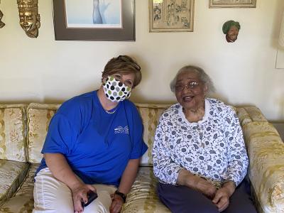 Photograph shows two people sitting on a couch in a living room. Heidi Rhea sits to the left of Evelyn Stafford. 