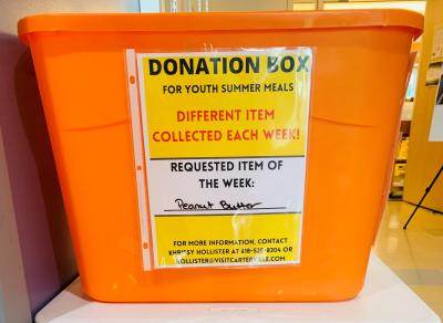 Photograph of bright orange donation box. Text on box reads: Donation Box for Youth Summer Meals 