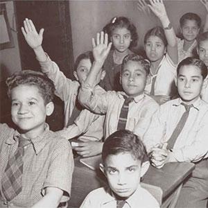 Children in desks raising hands (Library of Congress)
