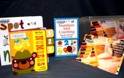 A plastic tub sits with with four book in front of it about learning numbers.