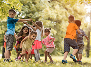 Two children stand across from each other and hold up their arms while grabbing hands to make a bridge for other children to run under while playing outside.