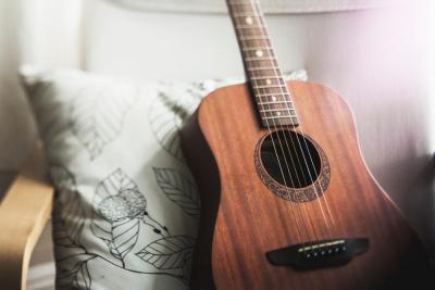 A wooden guitar sitting on a chair with a green pillow behind it.