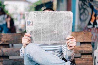 Man reading newspaper on park bench