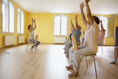 Group of senior citizen women do chair yoga.