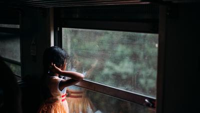 A shadowy photo of a girl looking out a window at some trees