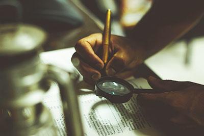 Person holding magnifying glass and taking notes in a book