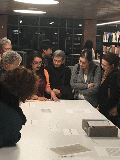 Person talking about an artifact on a table, with others gathered around