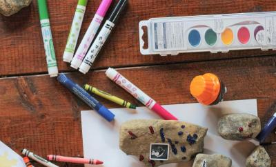 Photo of markers, crayons, paint on a table.