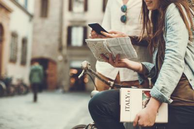 Woman sitting on a bike holding a map and book that says "Italy"