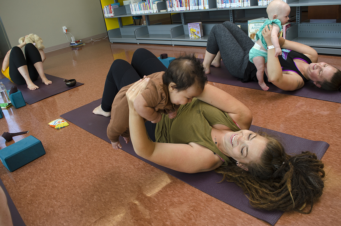 Mom laying down holding baby over her head on a yoga mat.