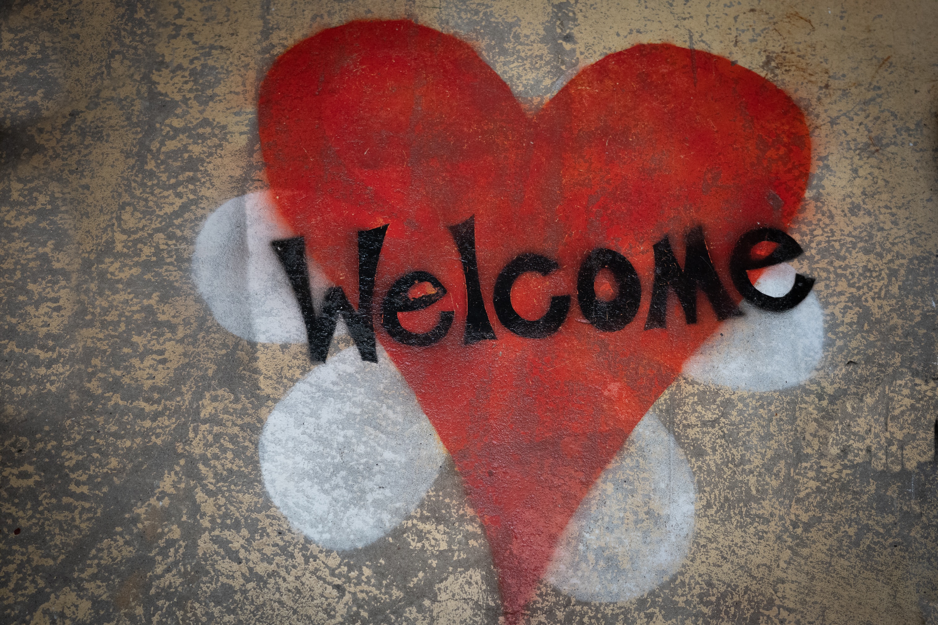 Photograph of a street art. The word welcome is written in black across a red heart.